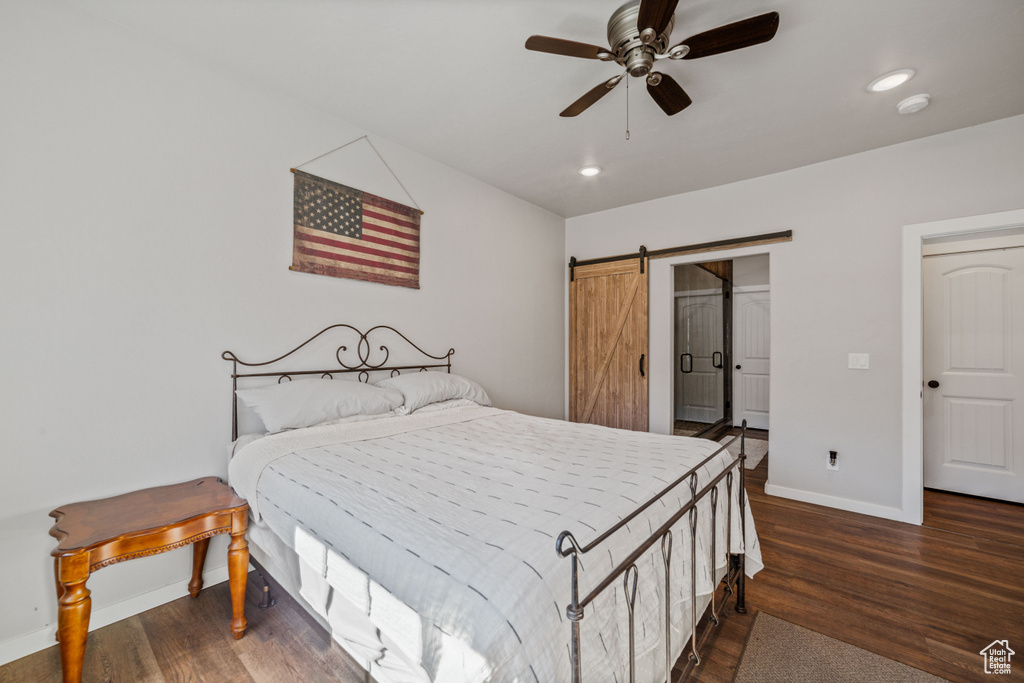 Bedroom featuring dark wood-type flooring, ceiling fan, and a barn door