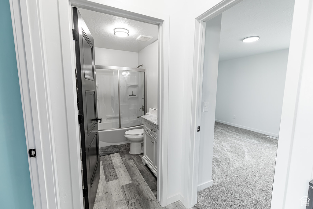Full bathroom with hardwood / wood-style flooring, a textured ceiling, enclosed tub / shower combo, vanity, and toilet