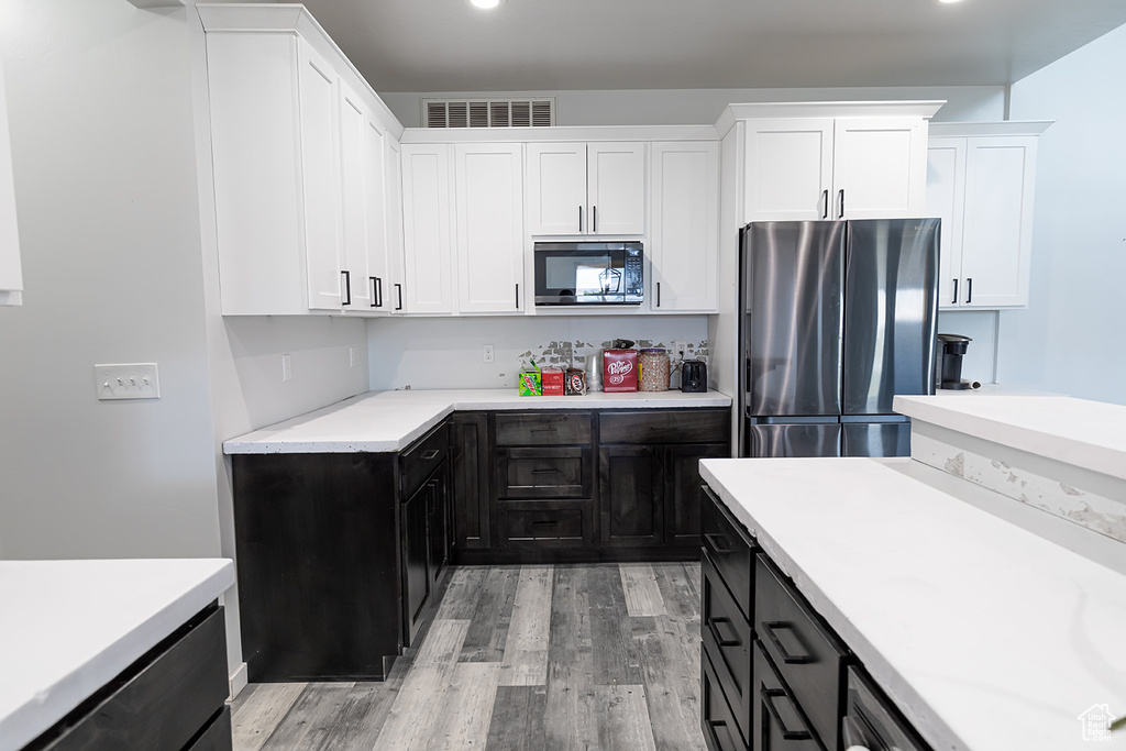 Kitchen with white cabinetry, black microwave, and stainless steel fridge