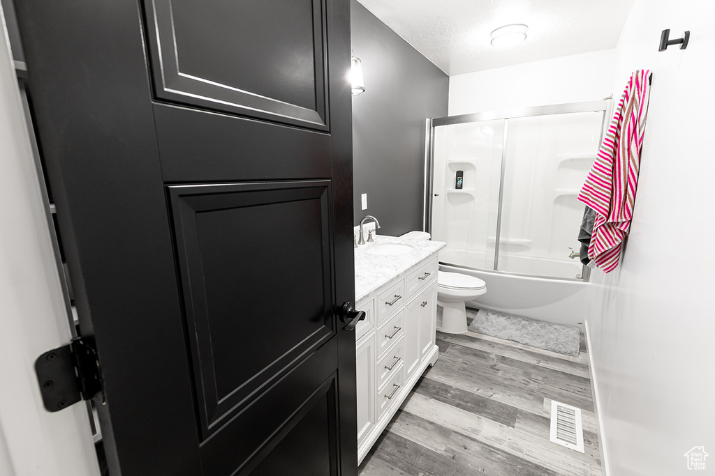 Full bathroom featuring bath / shower combo with glass door, hardwood / wood-style flooring, toilet, and vanity