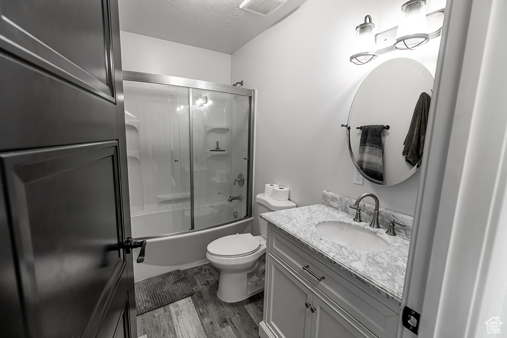 Full bathroom with bath / shower combo with glass door, a textured ceiling, toilet, wood-type flooring, and vanity