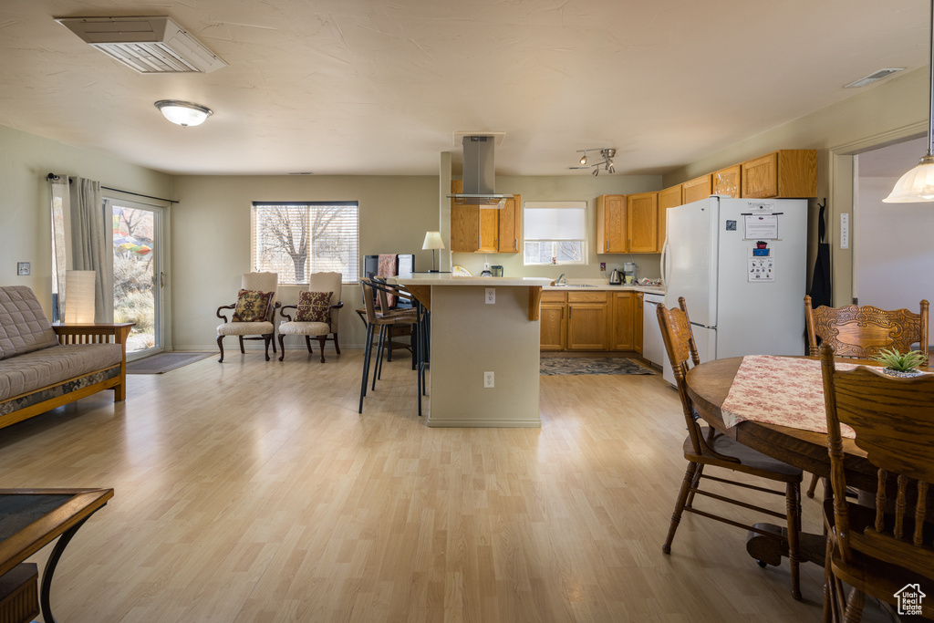 Kitchen with white fridge, decorative light fixtures, dishwasher, light hardwood / wood-style floors, and a breakfast bar