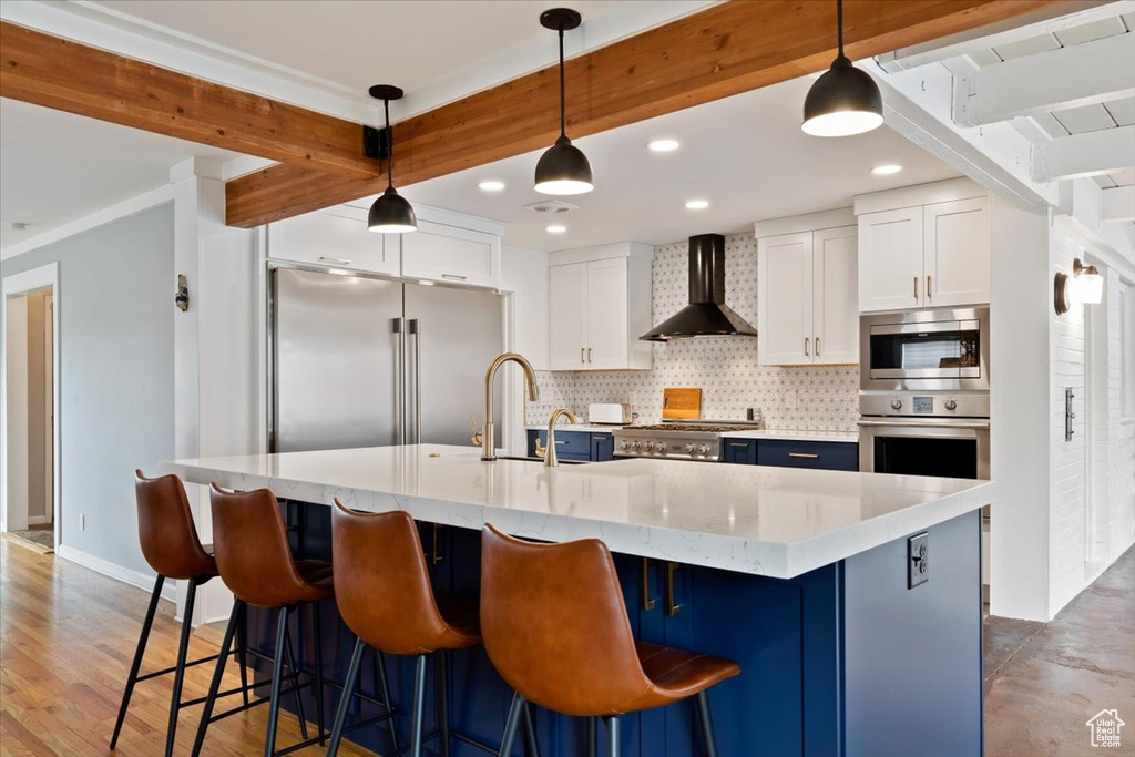 Kitchen featuring tasteful backsplash, wall chimney exhaust hood, appliances with stainless steel finishes, decorative light fixtures, and a breakfast bar area