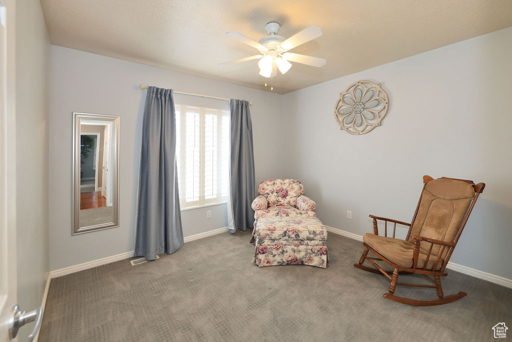 Living area featuring dark colored carpet and ceiling fan