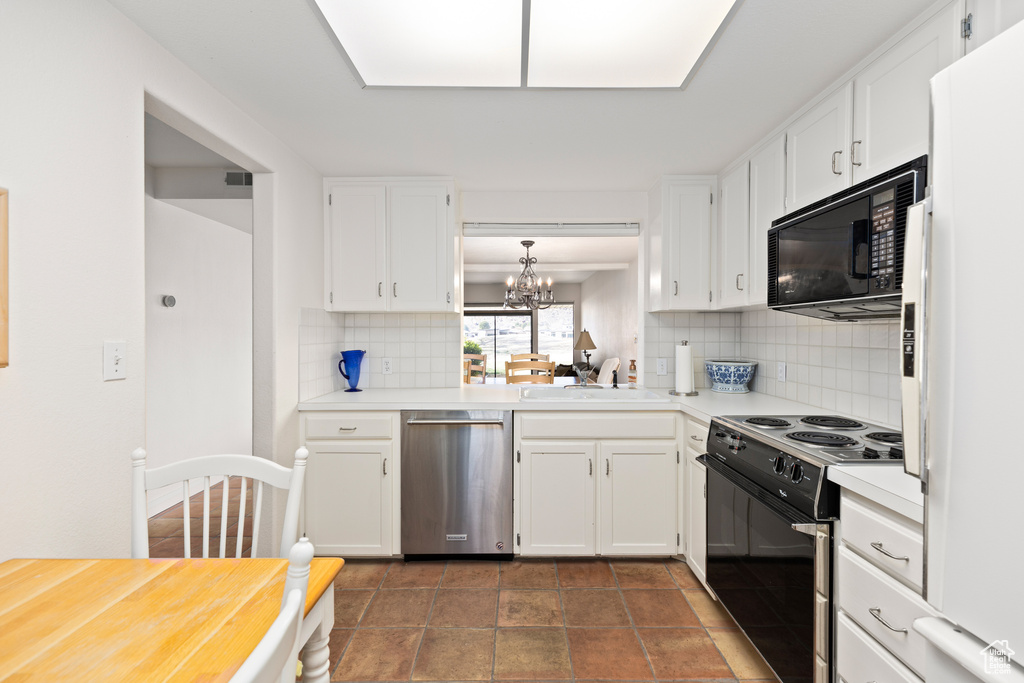 Kitchen featuring tasteful backsplash, white appliances, dark tile flooring, an inviting chandelier, and white cabinets
