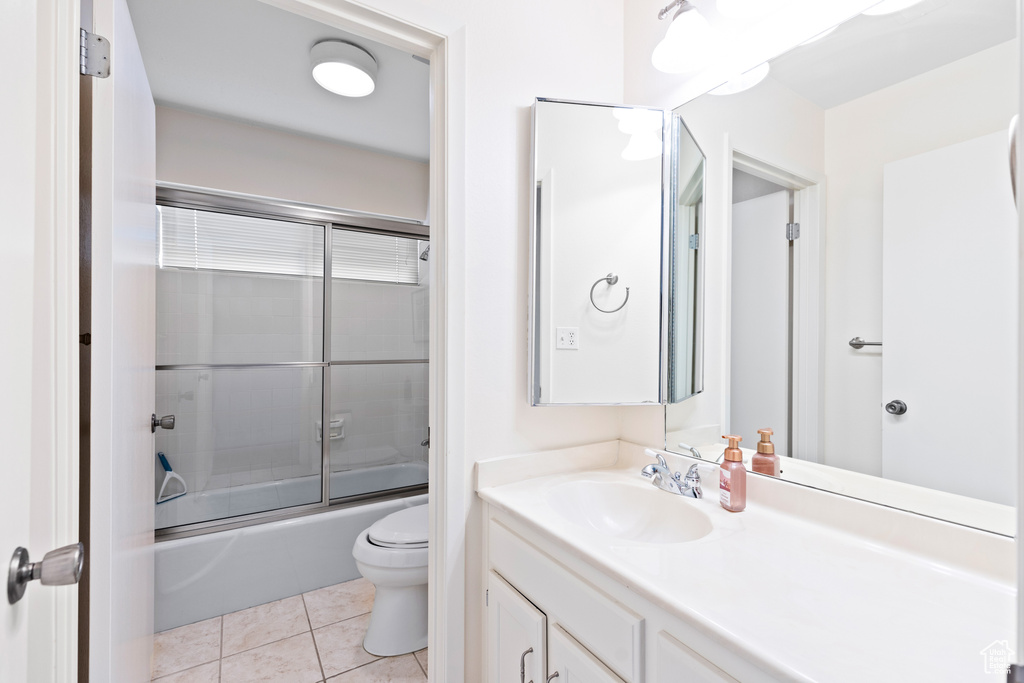 Full bathroom with tile flooring, bath / shower combo with glass door, toilet, and vanity