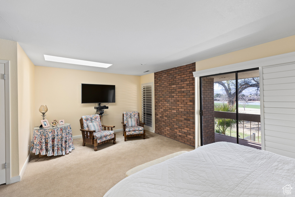 Bedroom featuring brick wall, light carpet, access to exterior, and a skylight