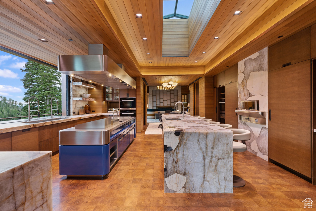Kitchen with an island with sink, light stone counters, a skylight, and a breakfast bar area