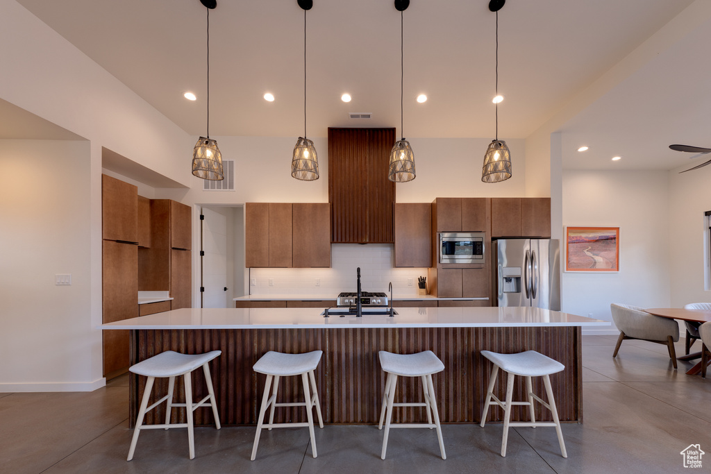 Kitchen featuring decorative light fixtures, backsplash, stainless steel appliances, and a kitchen island with sink