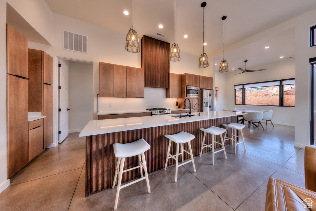 Kitchen with appliances with stainless steel finishes, a center island with sink, and hanging light fixtures
