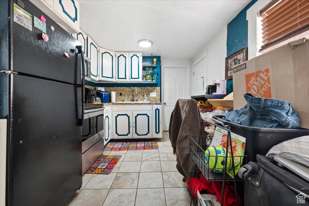 Kitchen with backsplash, black fridge, light tile floors, stove, and sink