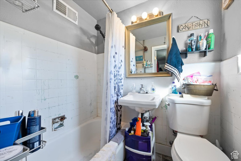 Full bathroom with tile walls, toilet, sink, and shower / tub combo