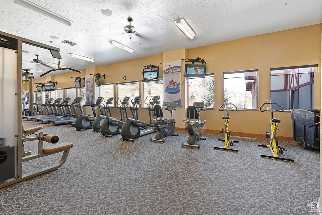 Gym with ceiling fan, a textured ceiling, and dark carpet