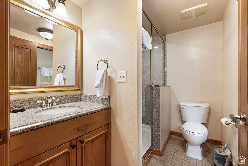 Bathroom with tile flooring, vanity with extensive cabinet space, toilet, and a shower with shower door