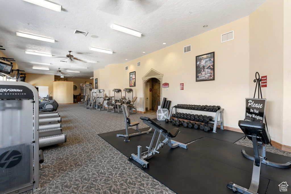 Exercise room featuring dark colored carpet, a textured ceiling, and ceiling fan