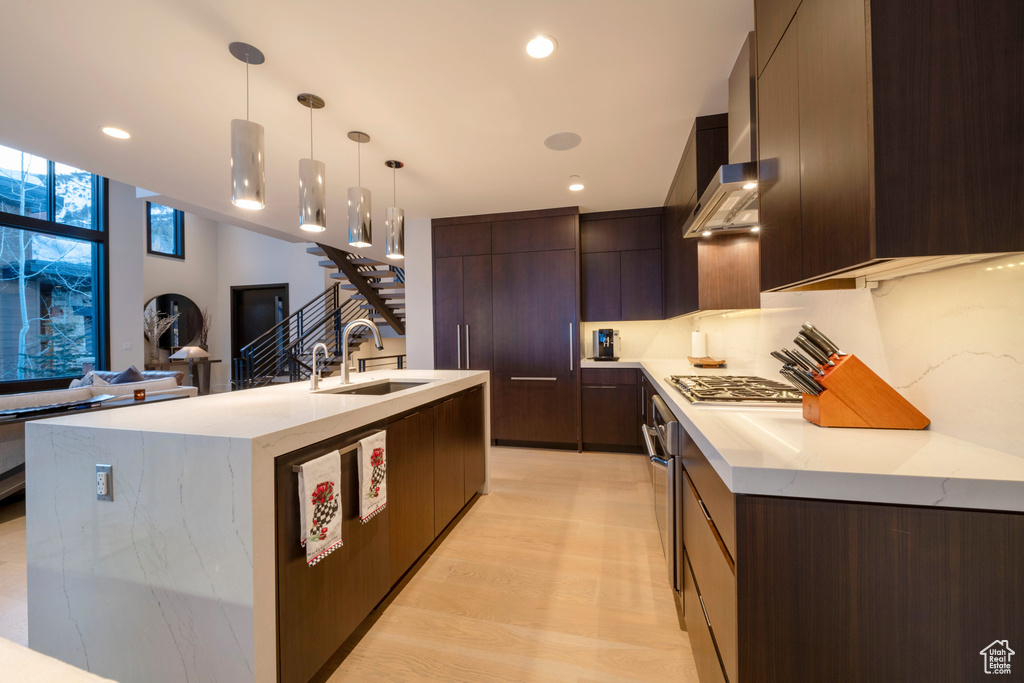 Kitchen featuring sink, decorative light fixtures, light hardwood / wood-style flooring, appliances with stainless steel finishes, and a center island with sink