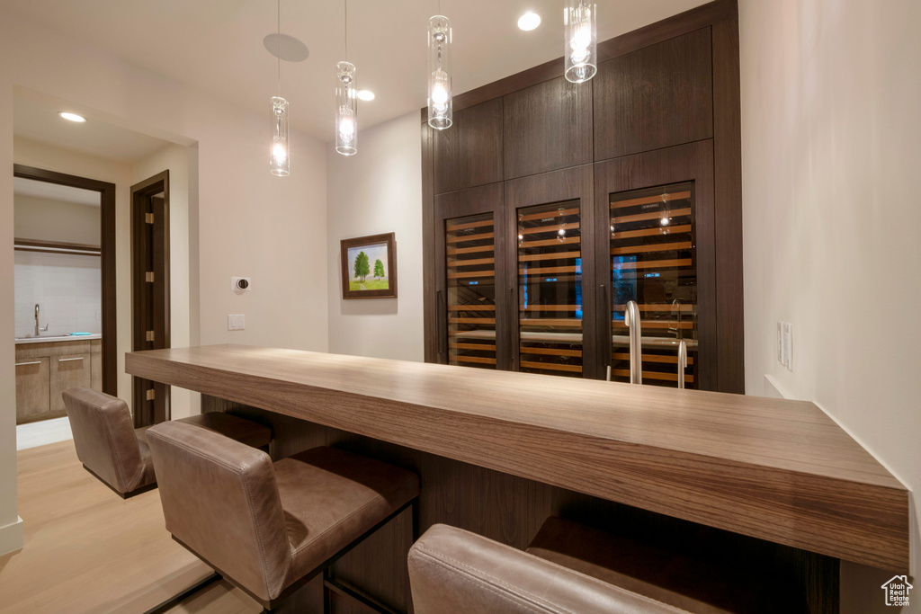 Bar featuring sink, light hardwood / wood-style floors, dark brown cabinetry, and decorative light fixtures