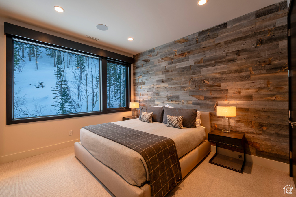 Bedroom featuring wooden walls, light carpet, and multiple windows