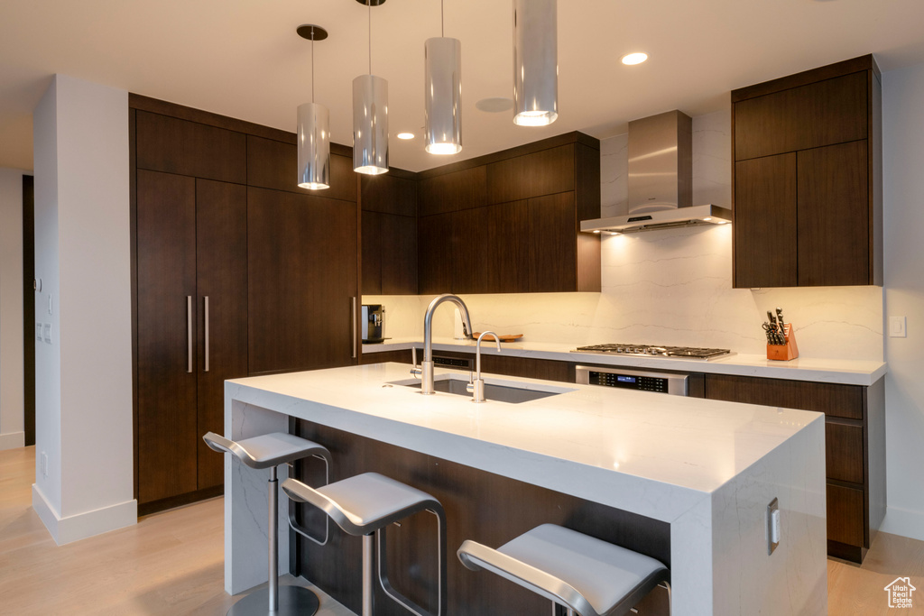 Kitchen with pendant lighting, a kitchen breakfast bar, wall chimney range hood, and light hardwood / wood-style flooring