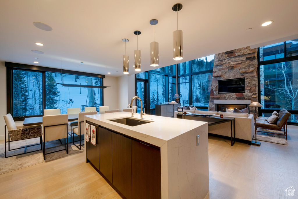 Kitchen featuring a center island with sink, light hardwood / wood-style floors, sink, decorative light fixtures, and a stone fireplace