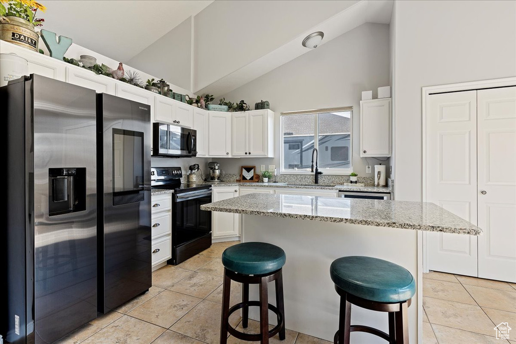 Kitchen with fridge with ice dispenser, sink, black / electric stove, a kitchen breakfast bar, and white cabinets