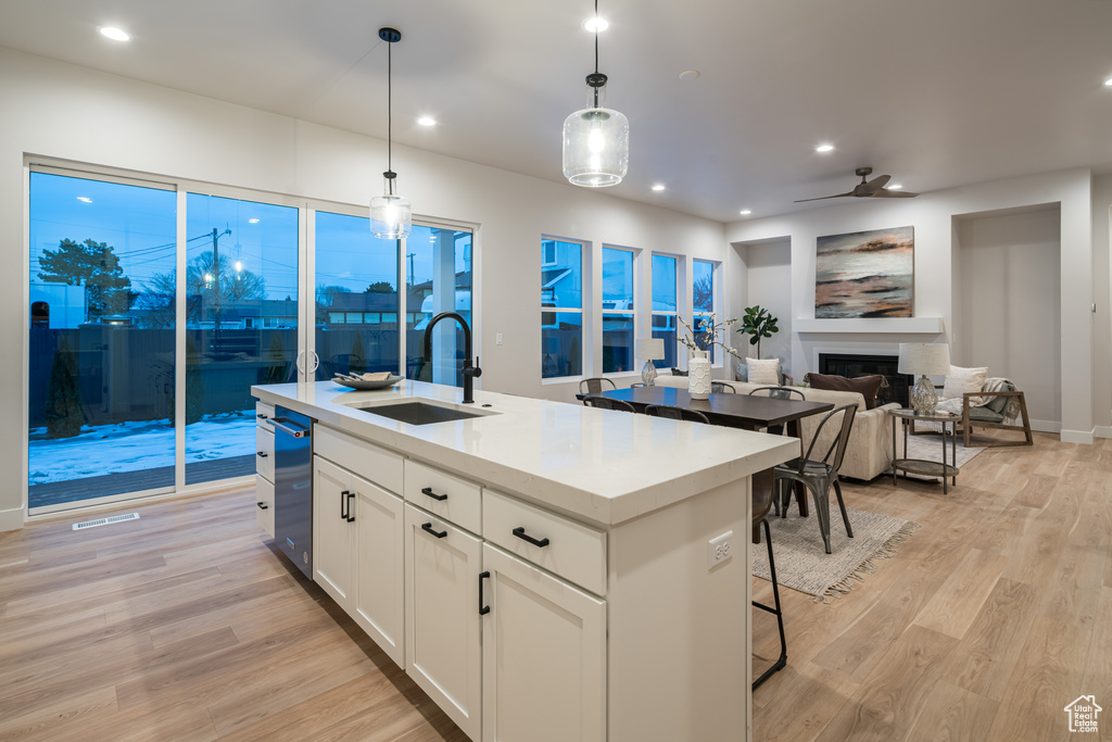 Kitchen with white cabinets, a center island with sink, sink, light hardwood / wood-style flooring, and pendant lighting