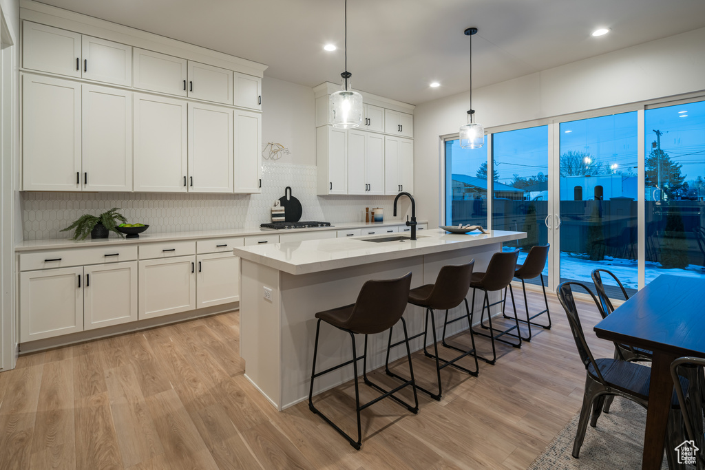 Kitchen featuring sink, white cabinets, pendant lighting, light hardwood / wood-style floors, and an island with sink