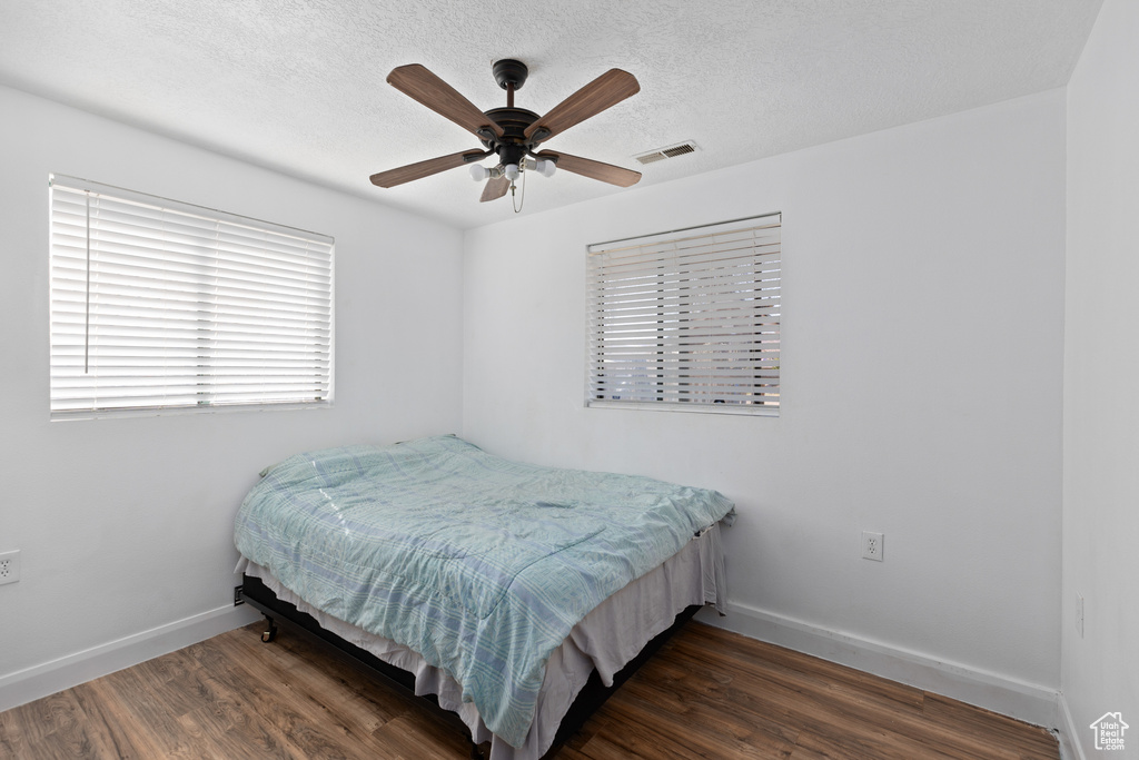 Bedroom with a textured ceiling, dark wood-type flooring, and ceiling fan