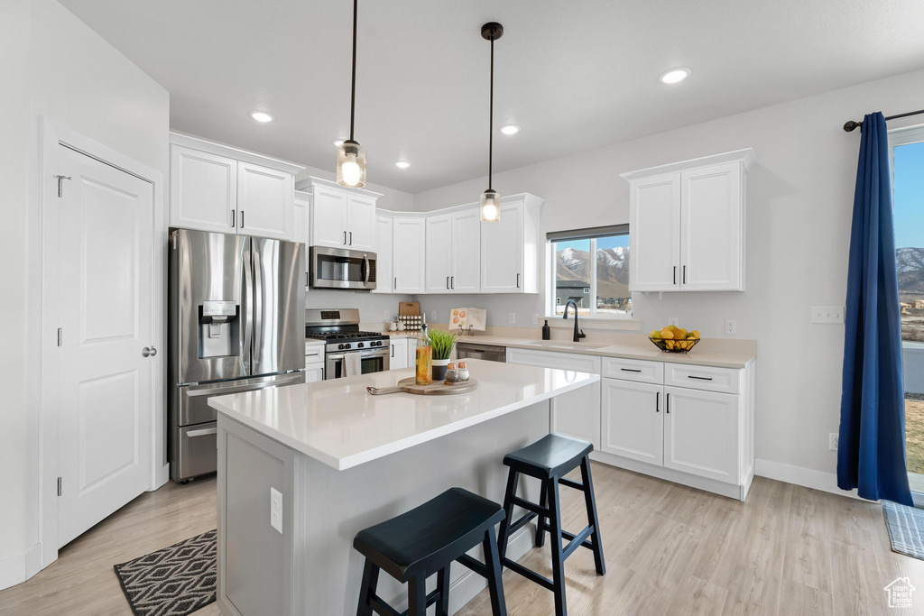 Kitchen featuring appliances with stainless steel finishes, a center island, decorative light fixtures, and light wood-type flooring