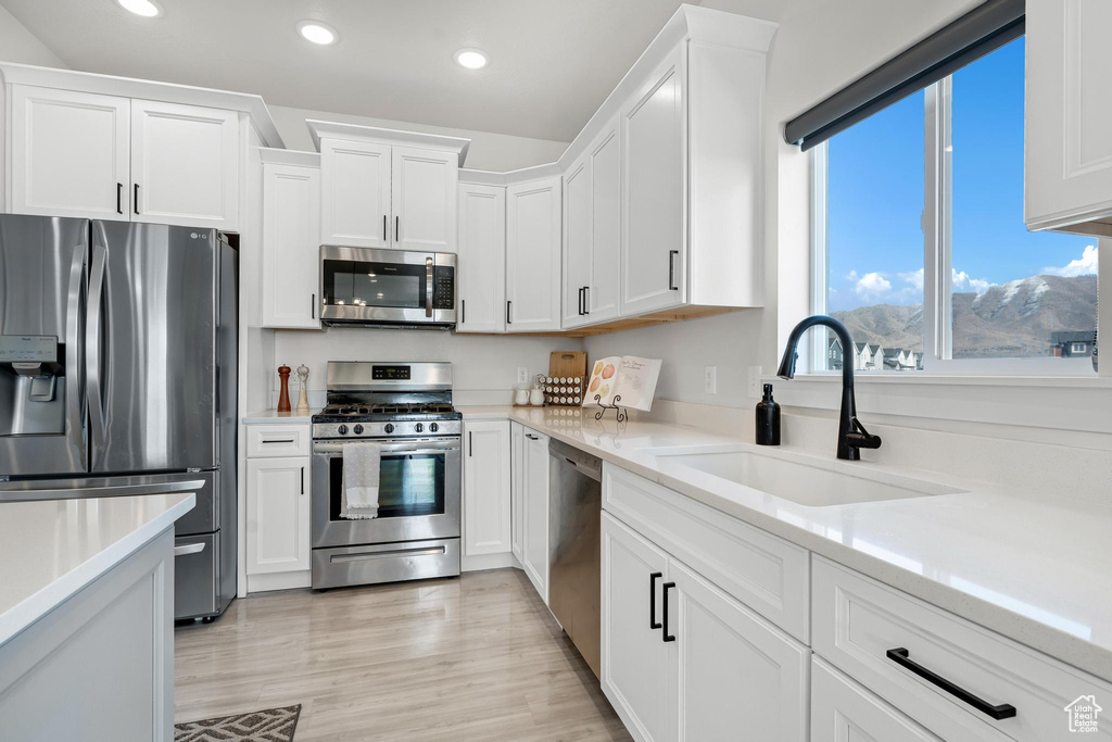 Kitchen with appliances with stainless steel finishes, white cabinetry, light hardwood / wood-style floors, and sink