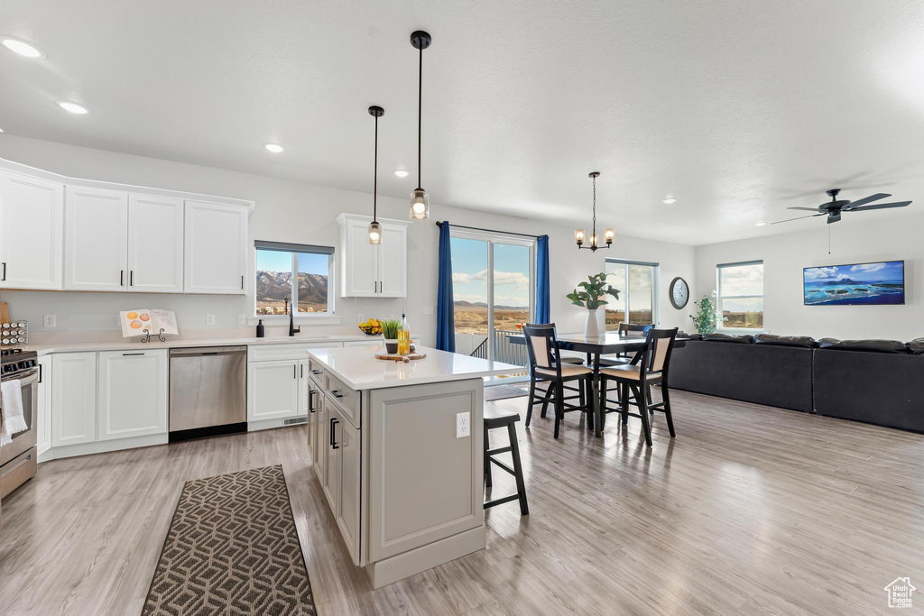 Kitchen with stainless steel appliances, ceiling fan with notable chandelier, a kitchen island, pendant lighting, and light wood-type flooring