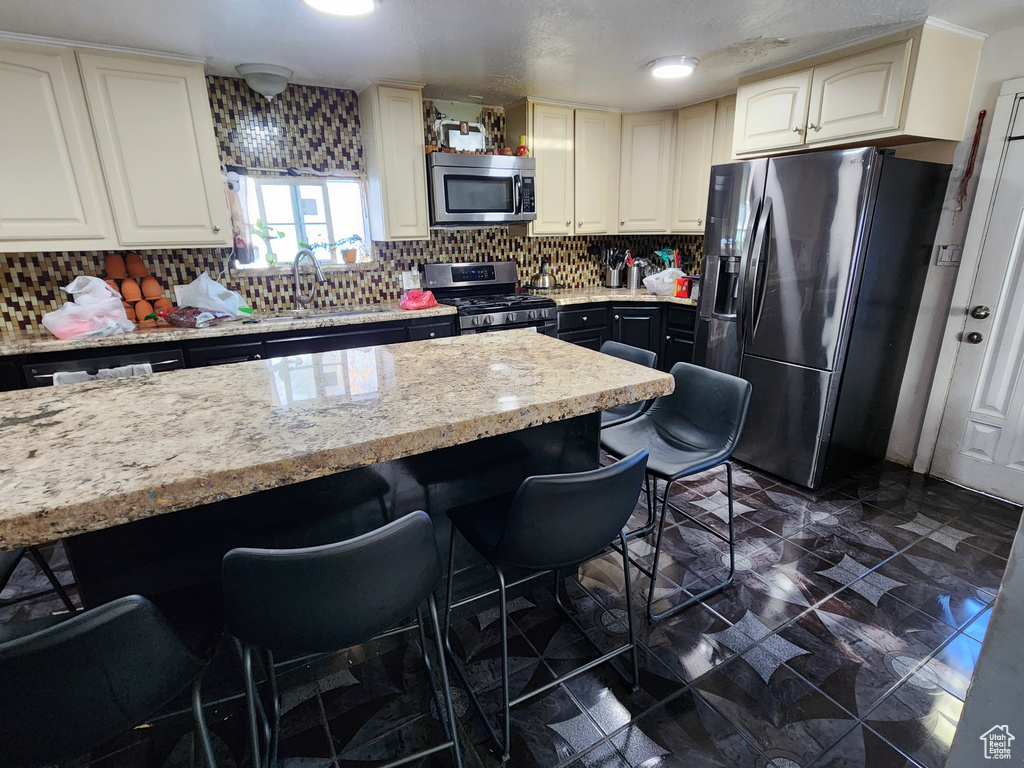 Kitchen with dark tile flooring, stainless steel appliances, a kitchen breakfast bar, and backsplash