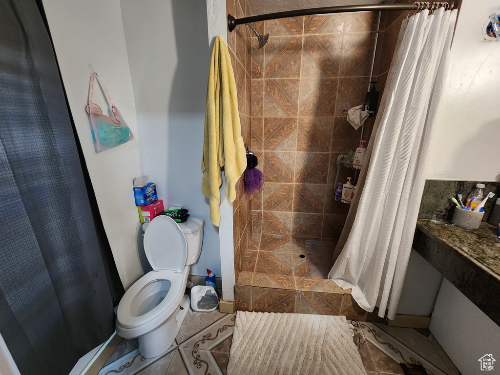 Bathroom featuring a shower with curtain, toilet, and tile floors