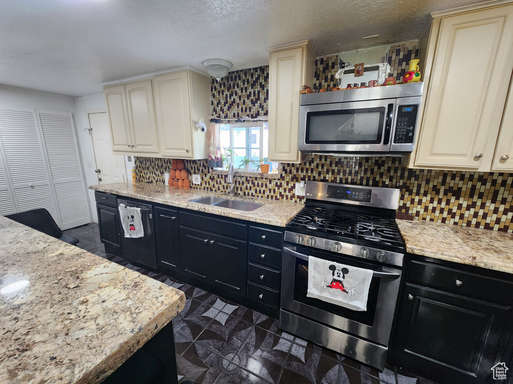 Kitchen featuring tasteful backsplash, appliances with stainless steel finishes, cream cabinetry, dark tile floors, and sink