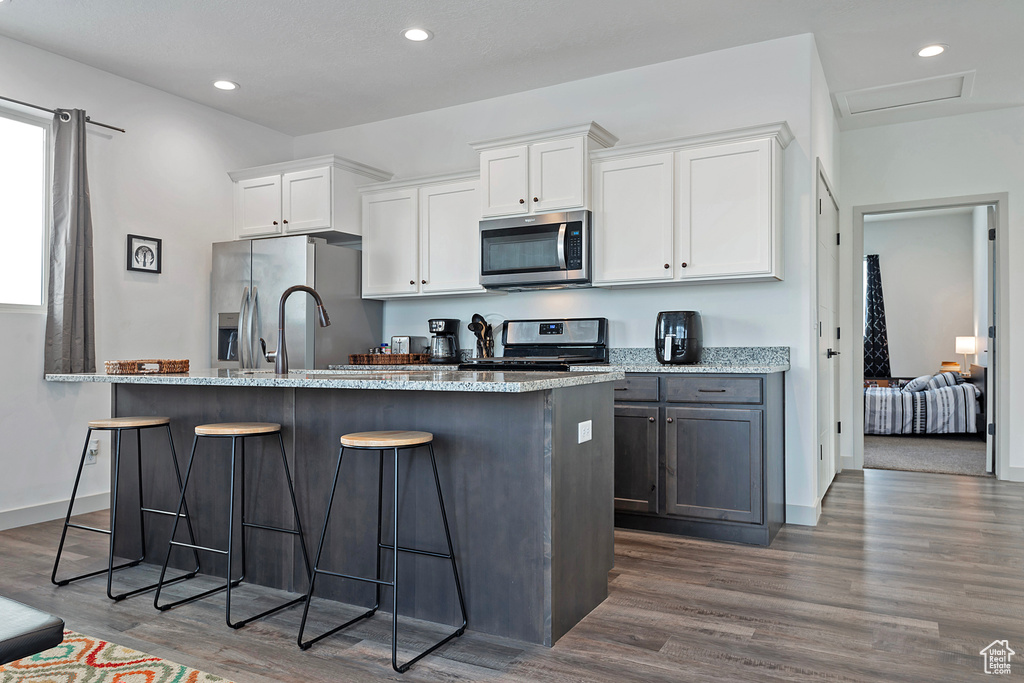 Kitchen featuring dark hardwood / wood-style flooring, light stone countertops, a kitchen breakfast bar, white cabinets, and stainless steel appliances