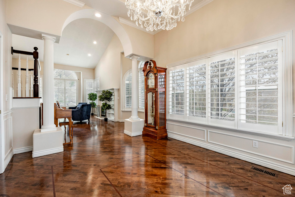 Foyer entrance with crown molding, ornate columns, dark hardwood / wood-style floors, and a notable chandelier