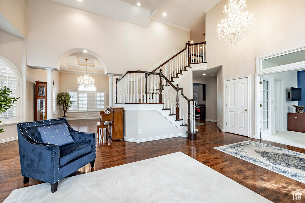 Entryway featuring a towering ceiling, a notable chandelier, crown molding, ornate columns, and dark hardwood / wood-style flooring