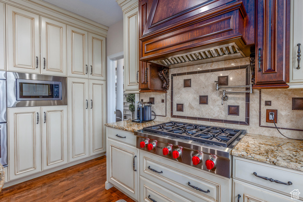 Kitchen featuring light stone counters, appliances with stainless steel finishes, custom exhaust hood, tasteful backsplash, and hardwood / wood-style flooring