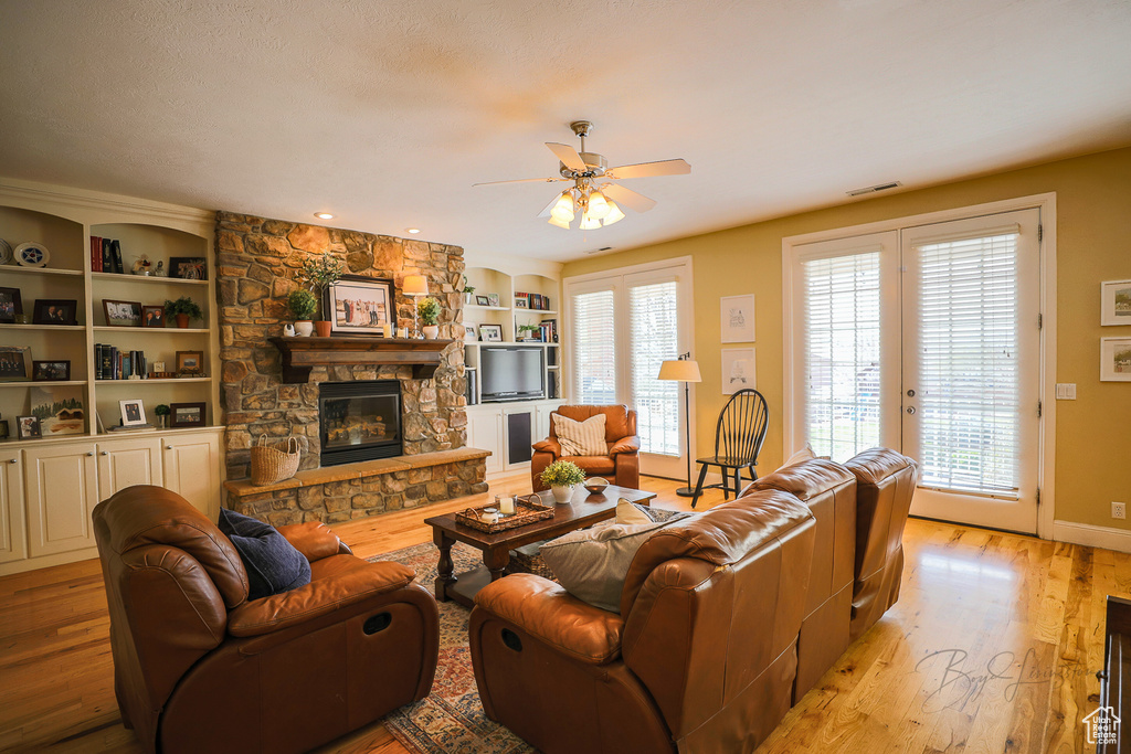 Living room with a stone fireplace, light wood-type flooring, plenty of natural light, and ceiling fan
