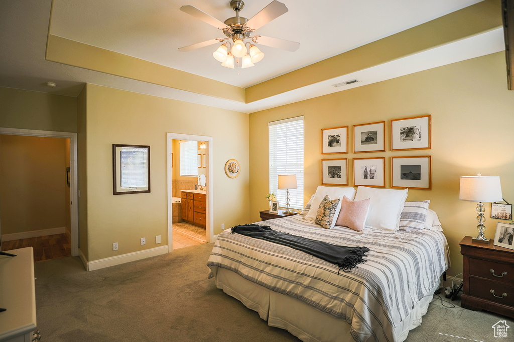 Carpeted bedroom with ensuite bathroom, ceiling fan, and a raised ceiling