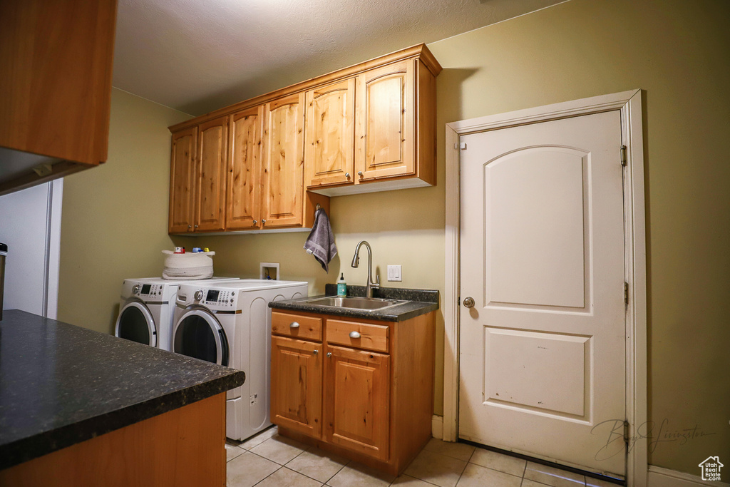 Laundry area with light tile floors, washing machine and dryer, cabinets, and sink