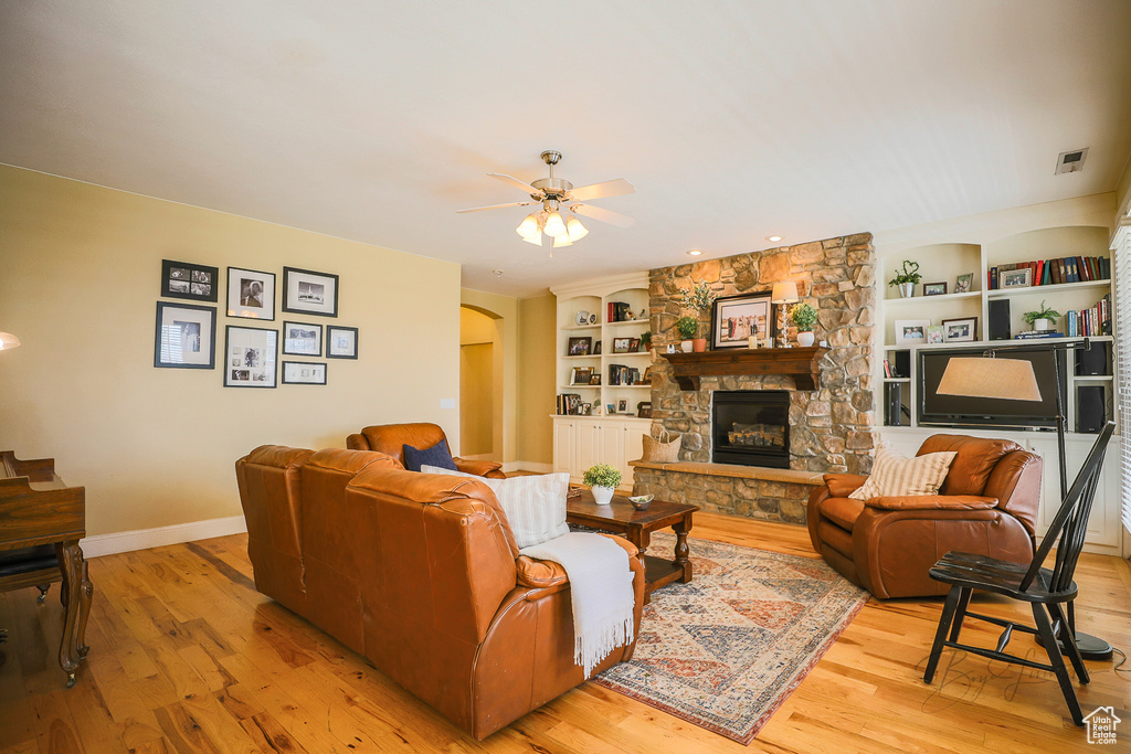 Living room featuring built in features, a stone fireplace, light hardwood / wood-style floors, and ceiling fan