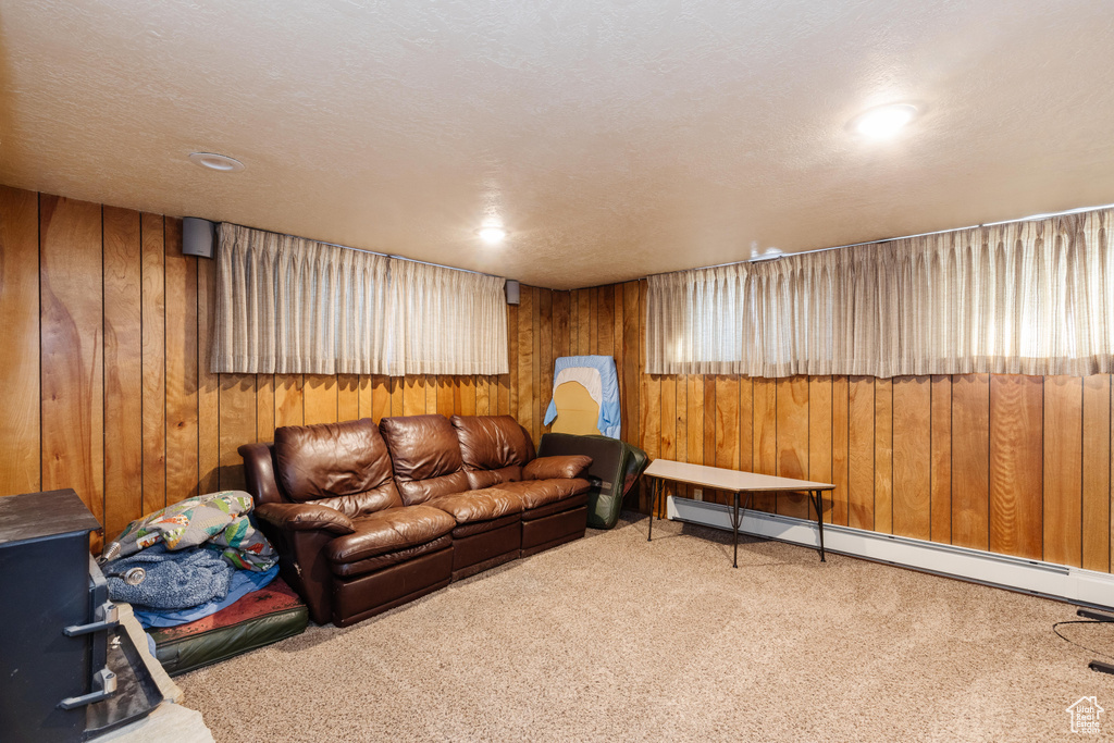 Carpeted living room with baseboard heating, a textured ceiling, and wooden walls