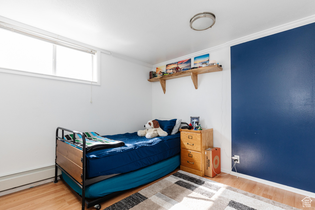 Bedroom featuring a baseboard radiator, ornamental molding, and light hardwood / wood-style floors
