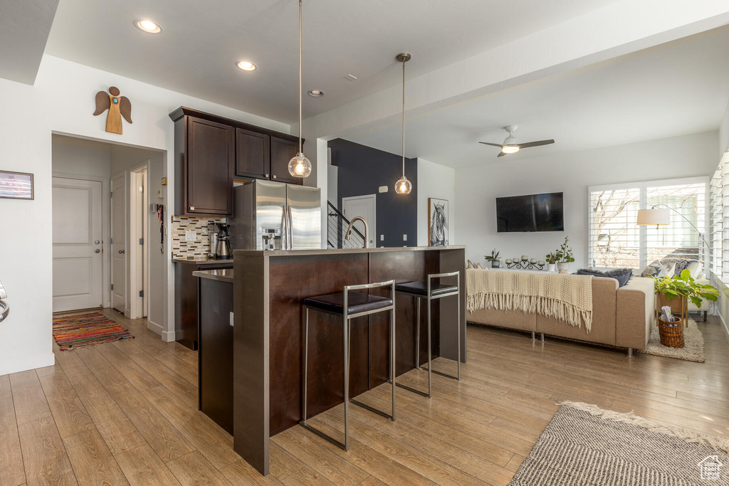 Kitchen with stainless steel fridge with ice dispenser, ceiling fan, a breakfast bar area, dark brown cabinetry, and light wood-type flooring