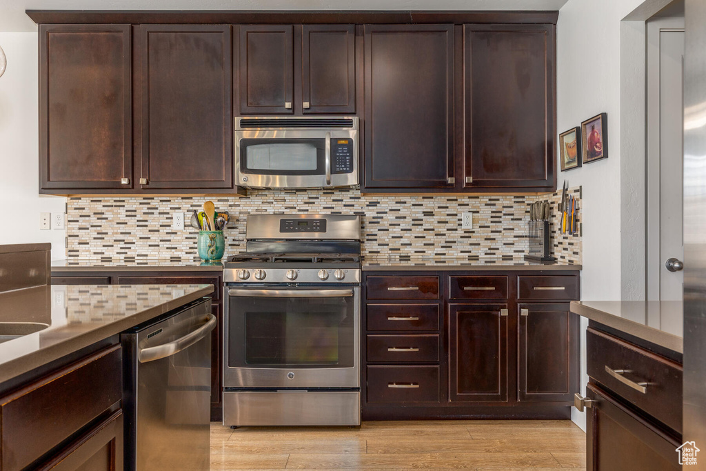 Kitchen with appliances with stainless steel finishes, light hardwood / wood-style flooring, dark brown cabinets, and backsplash