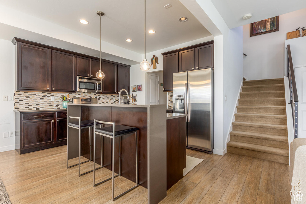 Kitchen featuring appliances with stainless steel finishes, light hardwood / wood-style flooring, a center island with sink, and decorative light fixtures