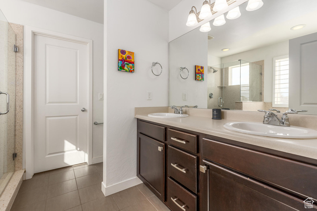 Bathroom featuring walk in shower, dual sinks, tile flooring, and vanity with extensive cabinet space