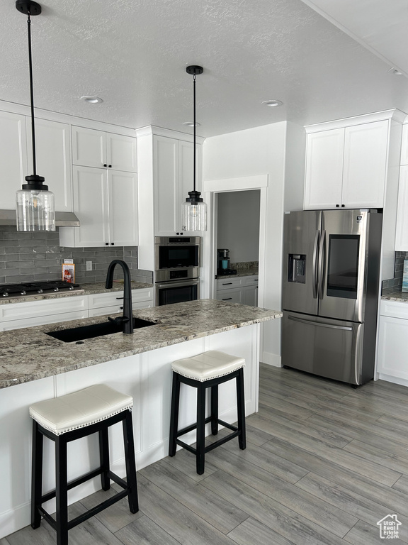 Kitchen featuring tasteful backsplash, sink, light stone countertops, white cabinetry, and stainless steel appliances