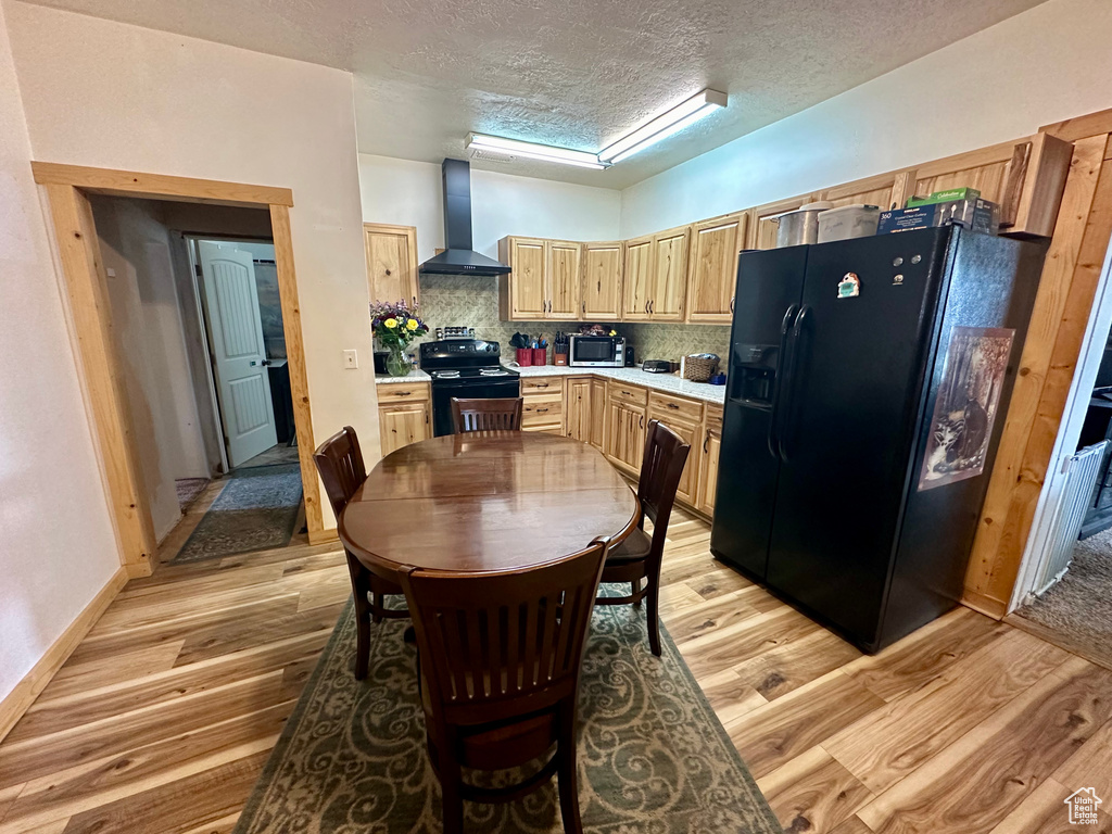 Kitchen featuring a textured ceiling, wall chimney range hood, tasteful backsplash, light wood-type flooring, and black appliances